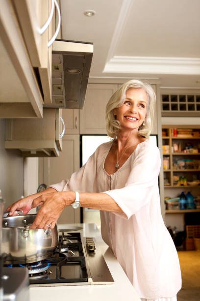 istock smiling older woman putting pot on stove 872772814