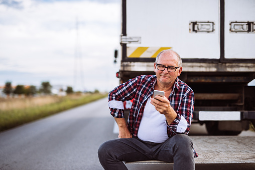 Senior truck driver checking his mobile phone.