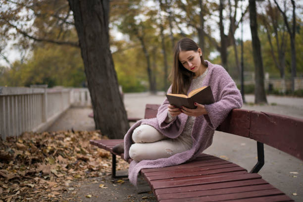istock Pretty young woman reading a book on a bench 872810994
