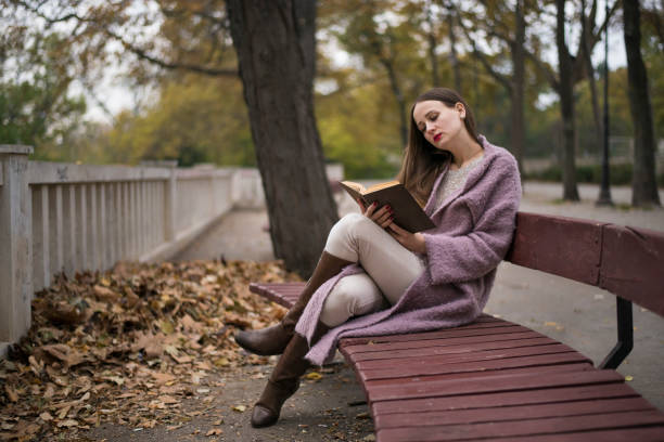 istock Cute young woman reading a book on a bench 872811092