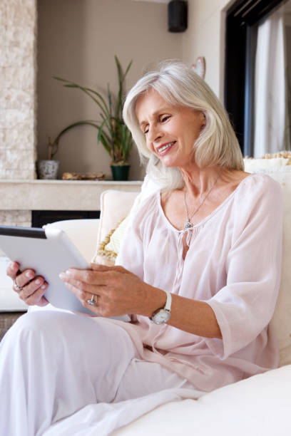 istock older woman smiling sitting on couch with tablet 872814280