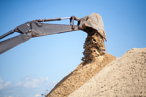 Un cubo del excavador grande de hierro recoge y vierte escombros arena y piedras en una cantera en la construcción de instalaciones de carretera photo
