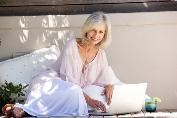 istock smiling older woman sitting outside with laptop 872814748