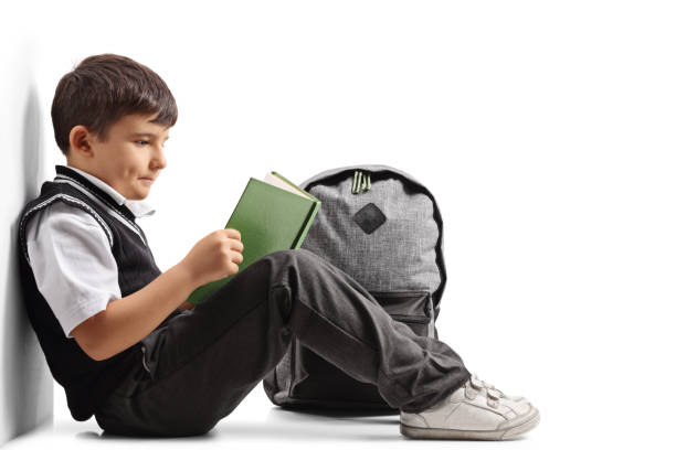 istock Little schoolboy seated on the floor reading a book 872832844