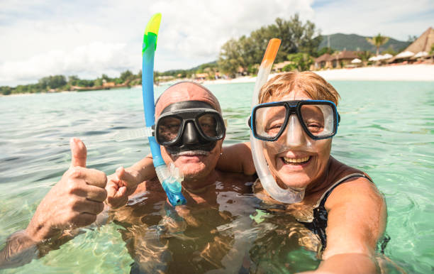 senior brautpaar nehmen selfie im tropischen meer ausflug mit wasser kamera - bootsausflug schnorcheln in exotischen szenarien - aktiv im ruhestand älterer und spaß-konzept auf der ganzen welt - warme helle filter - schwimmen fotos stock-fotos und bilder