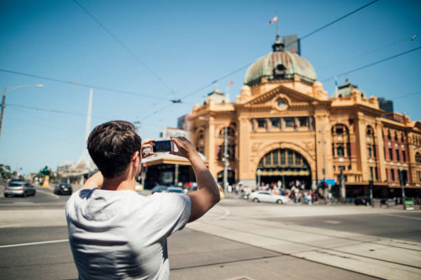 Taking A Photo Of Flinders Street Station Millennial tourist is using his smart phone to take a photo of Flinders Street Train Station in Melbourne, Victoria. victoria australia photos stock pictures, royalty-free photos & images