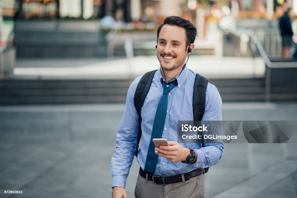 Millennial Businessman Commuting In Melbourne Happy millennial businessman is commuting in Melbourne, Victoria with a smartphone, listening to music through his earphones. Australia Stock Photo