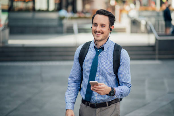 Millennial Businessman Commuting In Melbourne Happy millennial businessman is commuting in Melbourne, Victoria with a smartphone, listening to music through his earphones. day in the life stock pictures, royalty-free photos & images