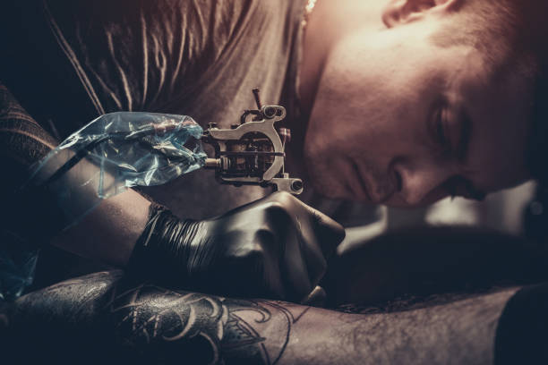 istock Tattoo master making tattoo on customer's leg 872843358