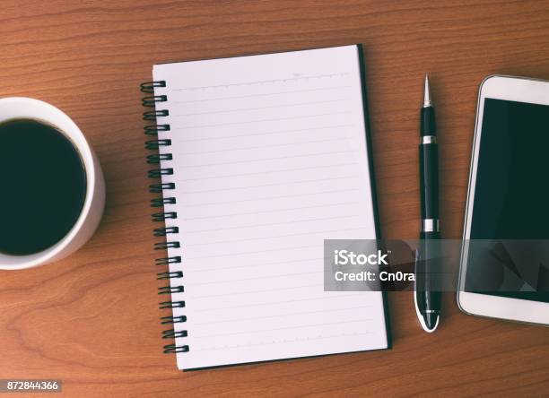 Directly Above Work Place With Open Note Pad Coffee Smartphone And Pen Stock Photo - Download Image Now