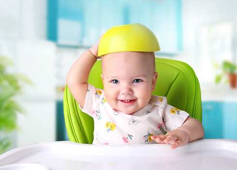 Baby food,nutrition concept.Child sitting at table with bowl over head.Kid girl eating.