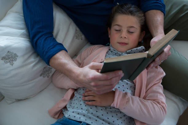 istock Girl sleeping while father reading book next to her 872858578