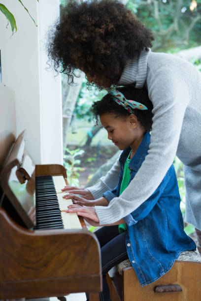 istock Mother assisting daughter in playing piano 872864952