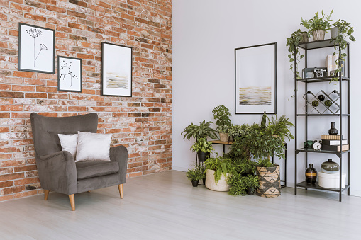 Poster on white wall above plants in simple living room with grey armchair against brick wall