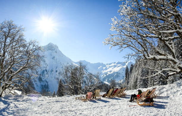 Group of people sitting with deck chairs in winter mountains. Sunbathing in snow. Germany, Bavaria, Allgau, Schwarzenberghuette. Group of people sitting with deck chairs in sunny winter mountains. Sunbathing in snow. Germany, Bavaria, Allgau, Schwarzenberghuette. apres ski stock pictures, royalty-free photos & images