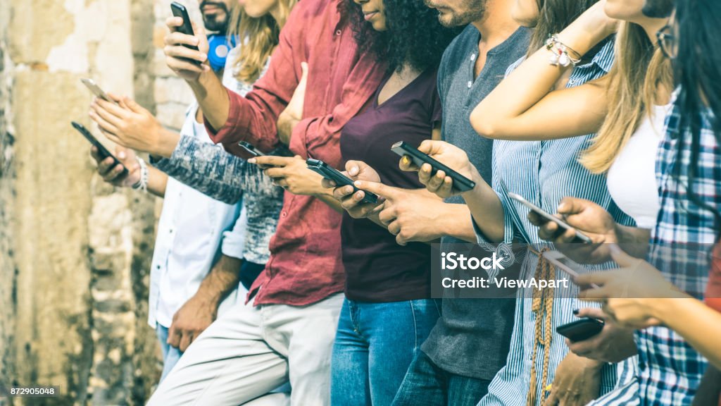 Group of multicultural friends using smartphone outdoors - People hands addicted by mobile smart phone - Technology concept with connected men and women - Shallow depth of field on vintage filter tone Social Media Stock Photo