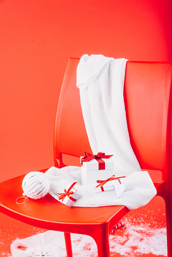 Christmas gift boxes and festive decorations on white scarf on the red chair.