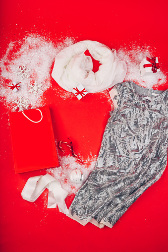 Festive Christmas attributes and decorations on a red background. Gift boxes and sequin dress on the snow. Red paper package.