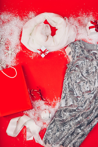 Festive Christmas attributes and decorations on a red background. Gift boxes and sequin dress on the snow. Red paper package.