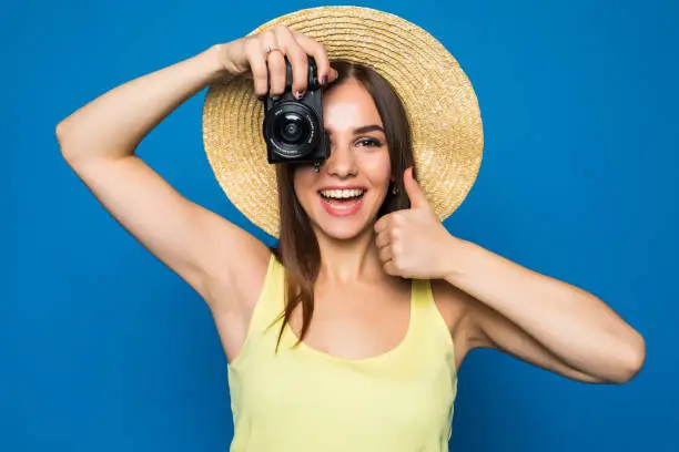 Close up photo of woman in hat on blue background taking a photo with digital camera