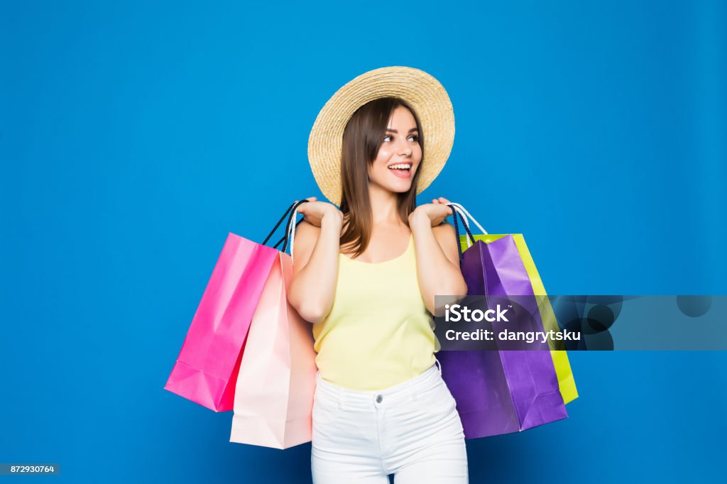 Ritratto di moda giovane donna sorridente che indossa una shopping bag, cappello di paglia su sfondo blu colorato - Foto stock royalty-free di Estate