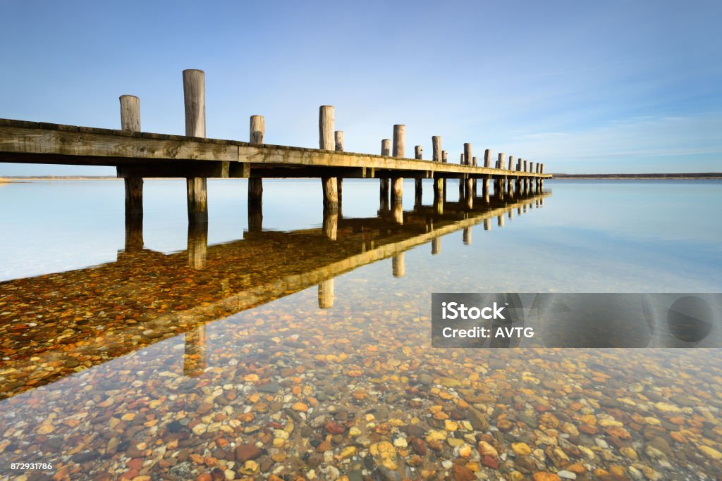 Calm clear lake with wooden pier Crystal clear water, pebbles on the bottom of the lake Atmosphere Stock Photo