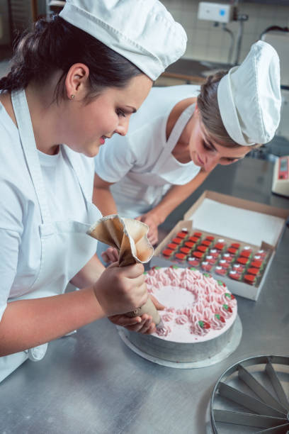istock Confectioner women putting cream on cake 872975900