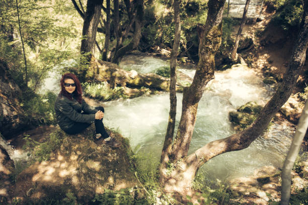 istock Enjoying in nature-woman sitting on tree branch by forest stream 872976274