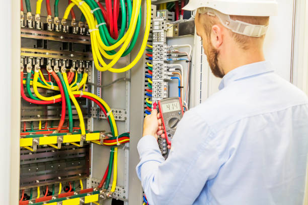 istock Electrician engineer in white helmet tests power voltage panel of three phase circuit. Service engineer electric with multimeter. 872987910