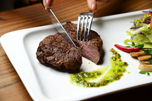 istock Hands cut medium rare beef steak with green dressing sauce pepper mushrooms and salad 873008614