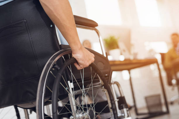 A disabled man is sitting in a wheelchair. A disabled man is sitting in a wheelchair. He holds his hands on the wheel. Nearby are his colleagues physical injury stock pictures, royalty-free photos & images