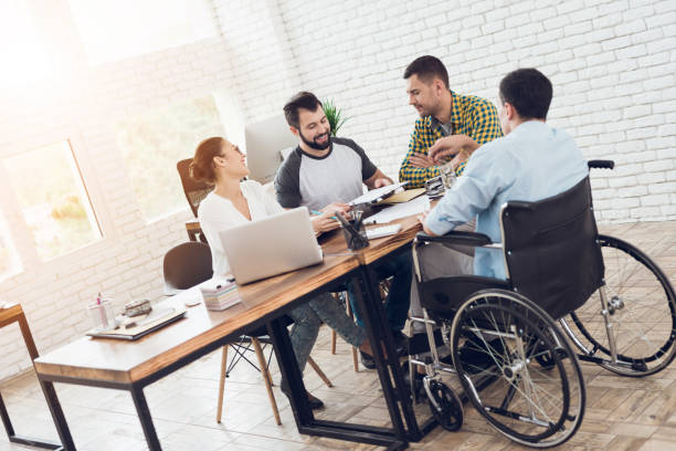 オフィス ワーカーと車椅子の人は、明るいオフィスで会話を作っています。 - working people physical impairment wheelchair ストックフォトと画像