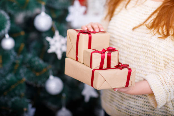 istock Woman's hands hold a New Year present on the background of a Christmas tree. 873022706