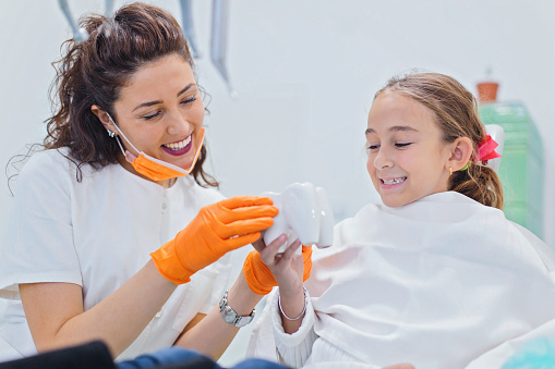 Smiling girl sitting in dentist chair with her pediatric dentist showing her teeth model. Dentistry, oral hygiene concept