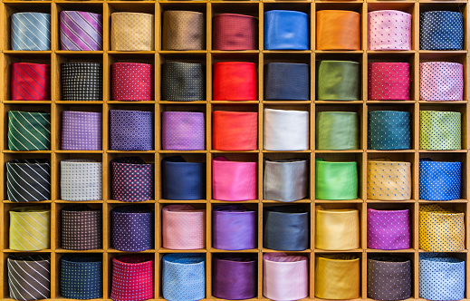 Showcase with multicolored ties. View of different colors ties in showcase. Multicolored man. Showcase of rolled neckties at store. Coiled ties on shelf at shop. Twisted neckties beautifully stacked.