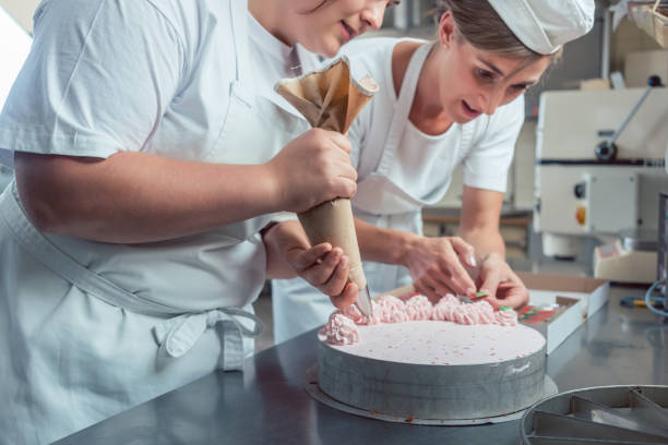 istock Confectioner women putting cream on cake 873039588