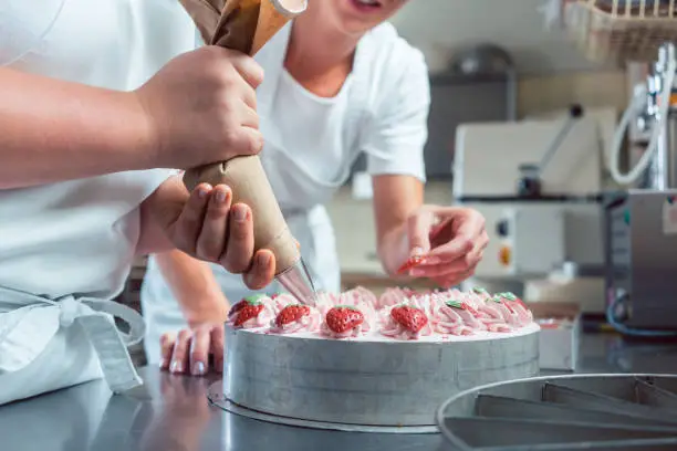 Confectioner or pastry chefs finishing cake with pastry bag, close-up on hands