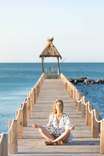 istock Young woman sitting on pier and practicing 873055238