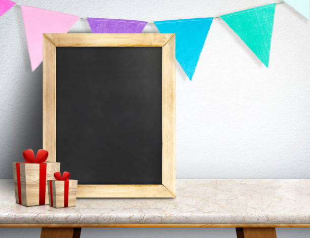 Blackboard with gift box and colorful flag banner on marble table at white wall,Leave space for display or montage of your design, Holiday new year concept