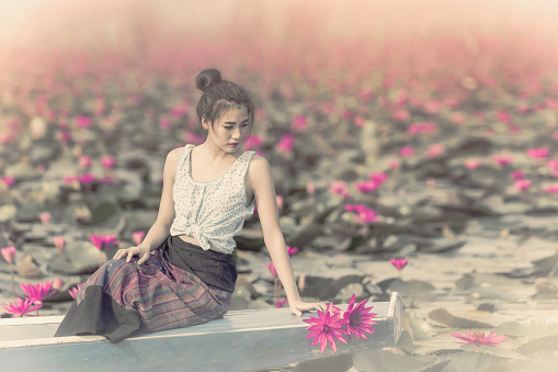Asian girl in the lake of lotus flowers,Woman wearing traditional,Thai people,Pretty girl with the sea of red lotus,Udon Thani,Thailand,Unseen Thailand,travel concept,The Lake of water lily in sunrise