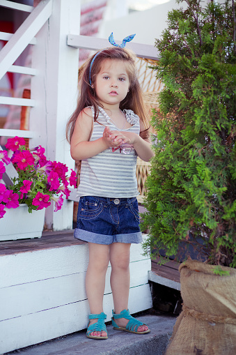 Stylish Beautifull Cute Baby Girl With Brunette Hair Posing On Wooden  Garden Full Of Flowers Wearing Tiny Jeans Shirts And Airy Skivy Underwaist  And Blue Sandals Stock Photo - Download Image Now -