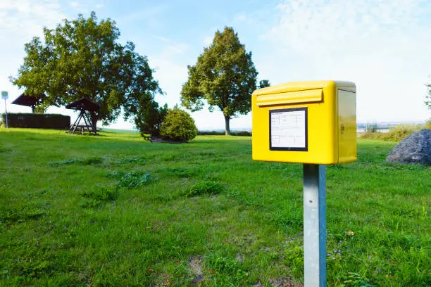 Yellow German postbox one in the green meadow with trees in village