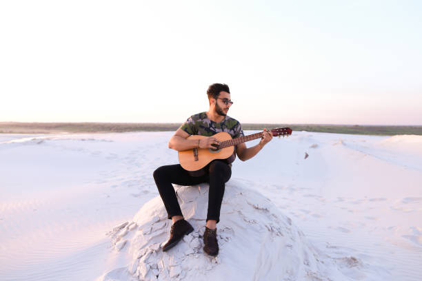 mignon jeune mâle arabe jouit de son de guitare, assis sur la colline à - musical instrument nature outdoors musician photos et images de collection