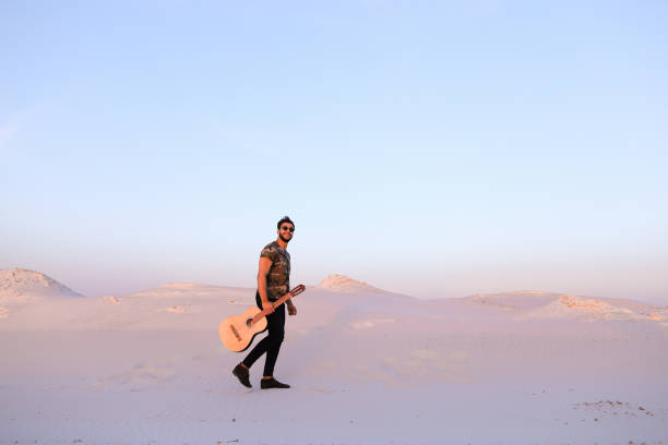 majestueux jeune homme musulman se promène avec guitare en mains par l’intermédiaire de dese - musical instrument nature outdoors musician photos et images de collection