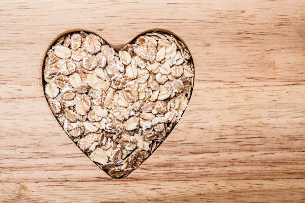cereal de aveia em forma de coração na superfície de madeira.   - oatmeal breakfast healthy eating cholesterol - fotografias e filmes do acervo