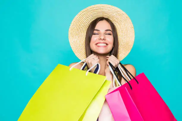 Photo of Portrait of young smiling european woman in hat with shopping bags on green background