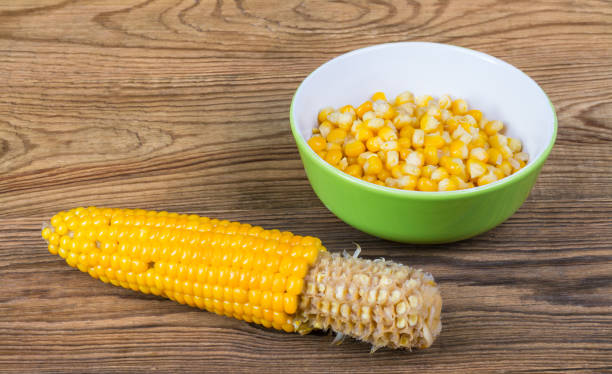 Partially empty corncob and heap of boiled maize in green bowl Yellow corn grains and partly gnawed cob on a wood background corn cob eaten stock pictures, royalty-free photos & images