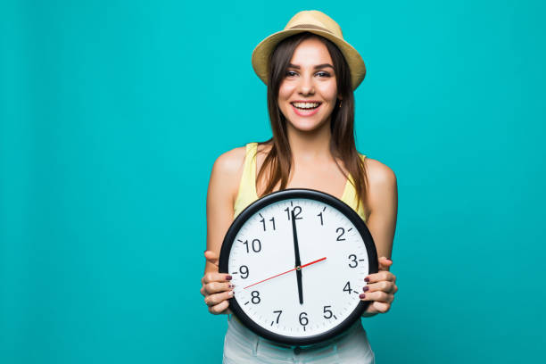 녹색 배경에 젊은 행복 한 여자 12 시계 들고 시계. 흰색 배경 위에 벽 시계와 긍정적인 예쁜 젊은 여자의 초상화 - 12 oclock 뉴스 사진 이미지