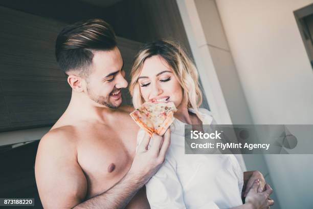 Boyfriend Feeding Girlfriend With A Slice Of Pizza While Hugging Her From Behind Stock Photo - Download Image Now