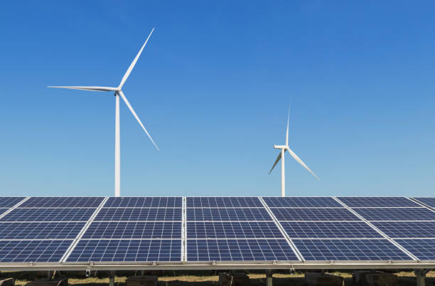 istock Rows array of  polycrystalline silicon solar panels and wind turbines generating electricity in hybrid power plant systems station with blue sky background 873195318